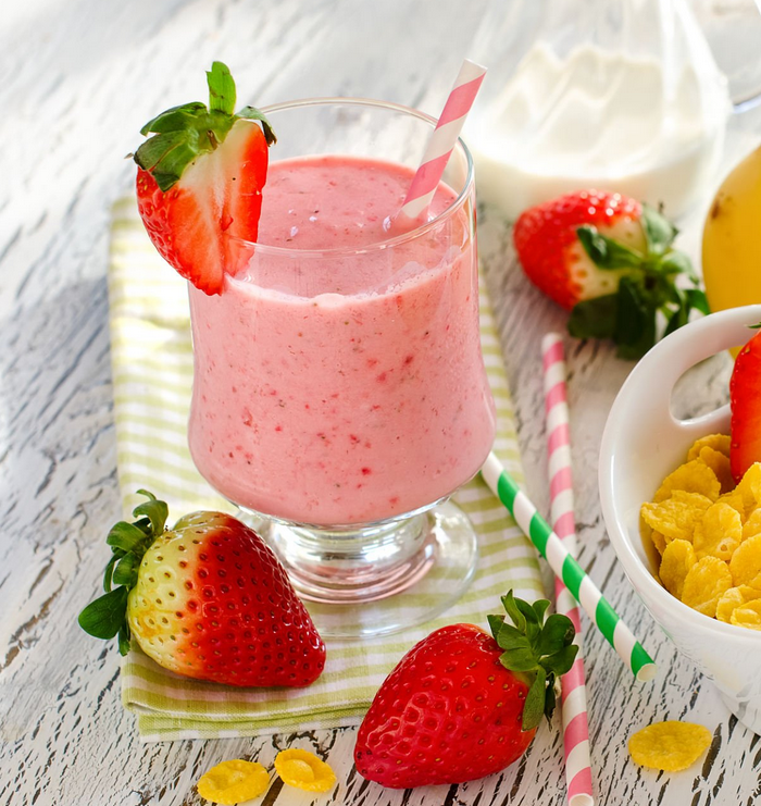Verre de smoothie jaune vif au curcuma, garni de rondelles de banane et de graines, posé sur une table en bois avec des ingrédients frais en arrière-plan.