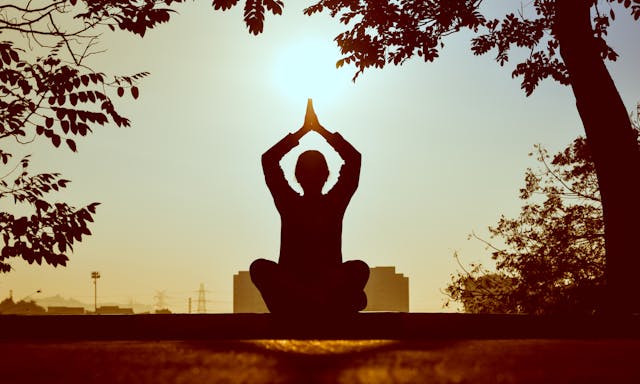 Femme assise en tailleur méditant au lever du soleil, en opposition à une autre pratiquant une posture de yoga, illustrant les deux approches pour réduire le stress