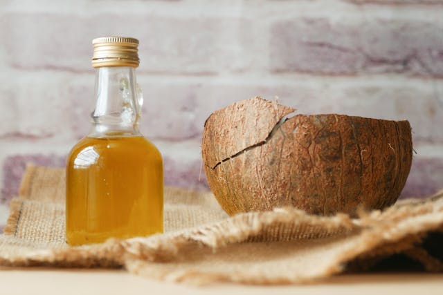 Bocal d’huile de coco posé sur une table en bois, entouré de noix de coco et d’éléments naturels